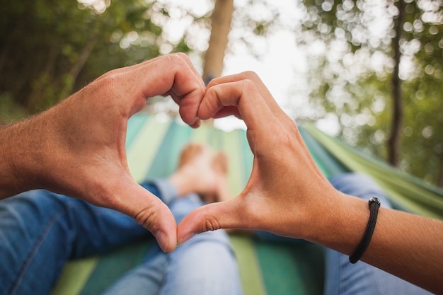 Couple lying in hammock making heart symbol