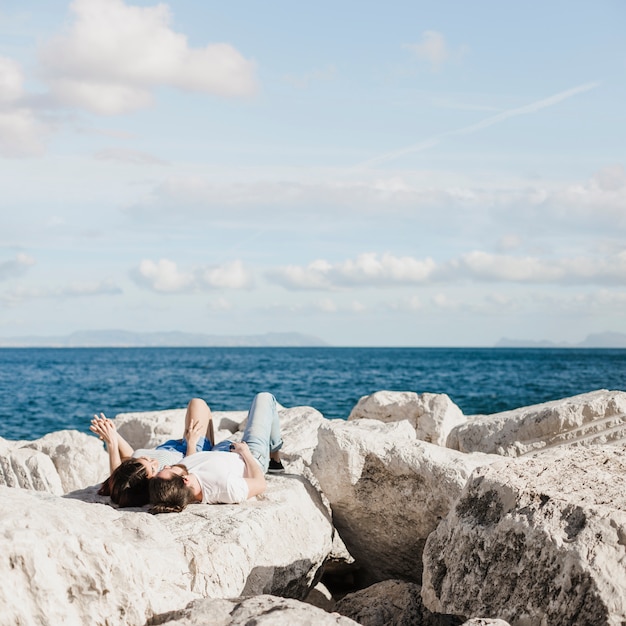 Free photo couple lying on rocks at the sea