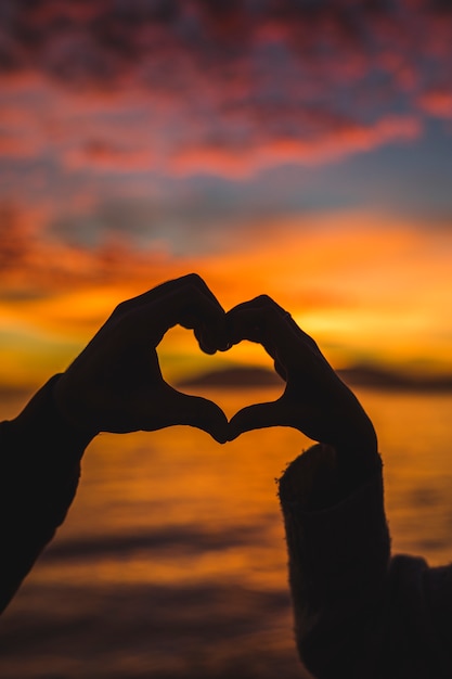 Couple making heart from hands on sea shore 