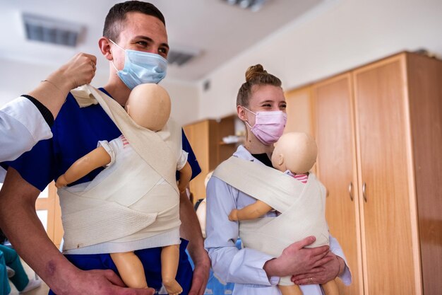 A couple of medical students learning how to attach a baby to themselves and smilling being helped