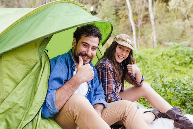 Couple near tent gesturing thumb-up