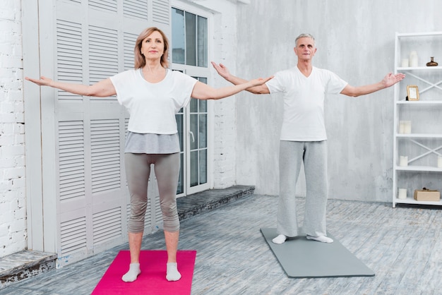 Free Photo couple performing yoga by outstretching arms standing on yoga mat