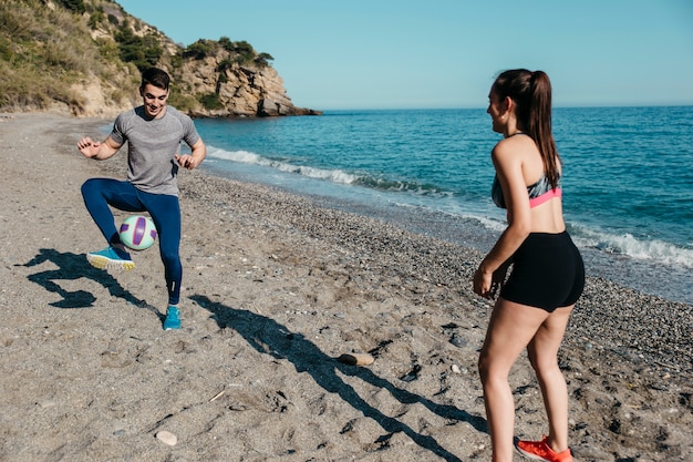 Free photo couple playing football at the beach