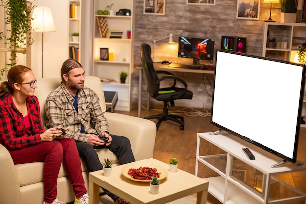 Couple playing video games on isolated white TV screen late at night in the living room