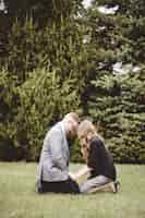 Free photo a couple praying together on their knees on a grassy lawn with trees in the background