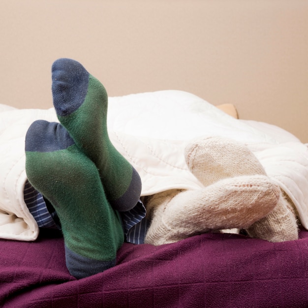 Free photo couple's feet wearing socks under the bed sheet