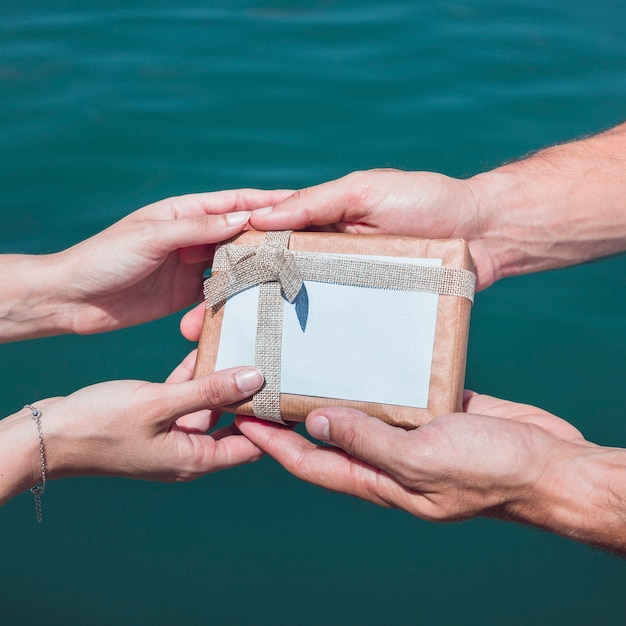 Free Photo couple's hand holding gift against sea water background