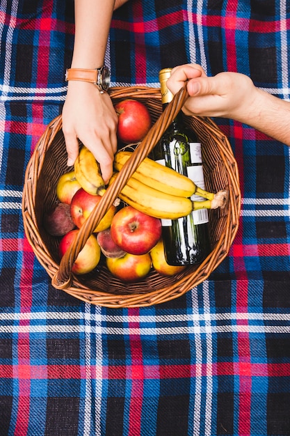 Free Photo couple's hand on picnic basket with fruits and champagne bottle