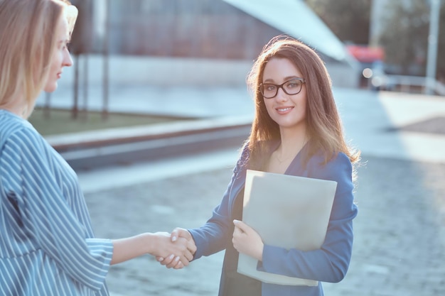 Free photo couple of serious businesswomen have unformal meeting outside, they are greeting one each other with handshake.