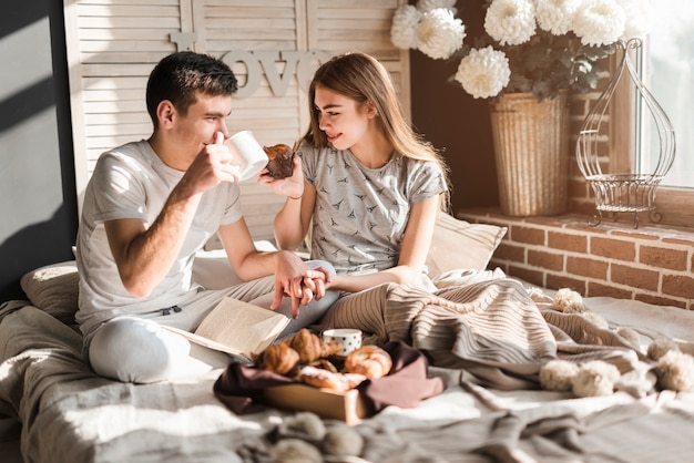 Couple sitting on bed holding each other's hand having breakfast together