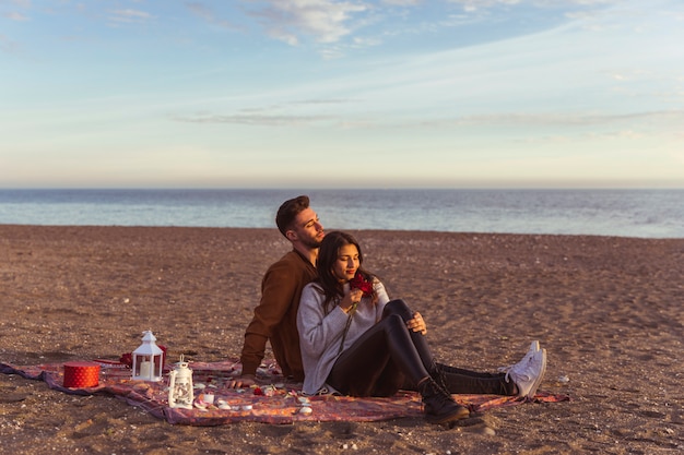 Free photo couple sitting on coverlet on sandy sea shore