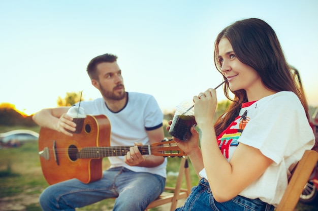 Free photo couple sitting and resting on the beach playing guitar on a summer day near river. love, happy family, vacation, travel, summer concept. caucasian man and woman