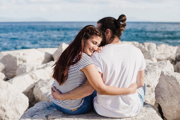 Couple sitting on rocks at the sea hugging