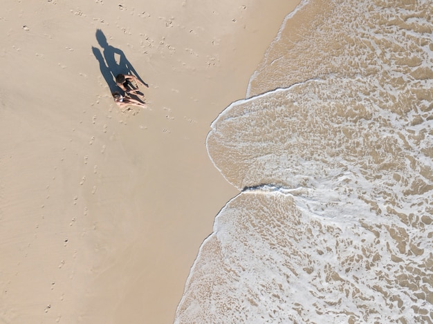 Free photo couple sitting on seashore close to foam waves