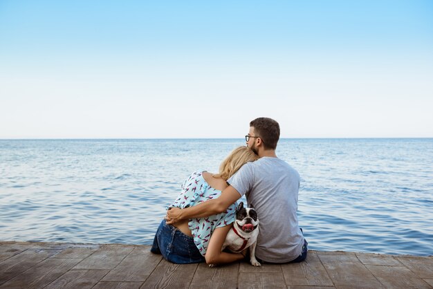 Free Photo couple sitting with french bulldog near sea