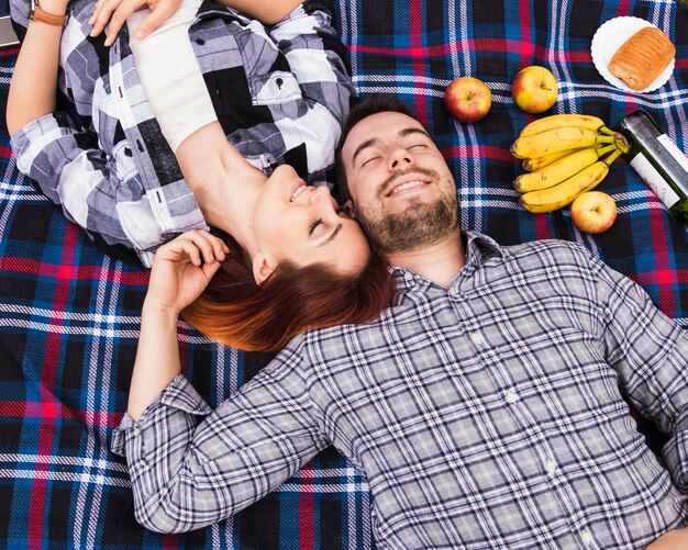 Couple sleeping on blanket with many fruits; puff pastry and champagne bottle