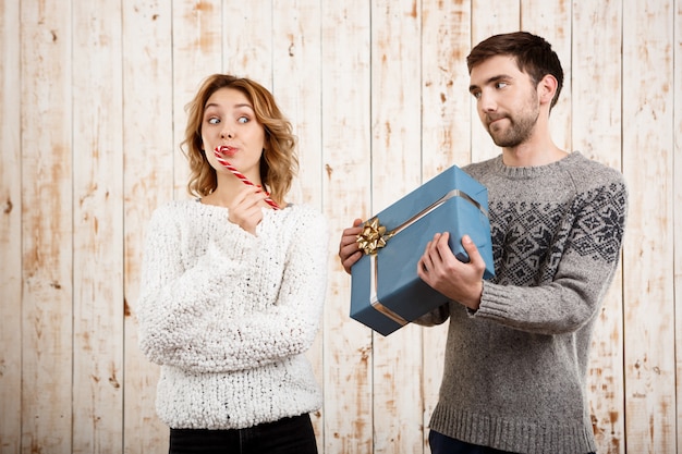 Couple smiling holding christmas candy and gift over wooden wall