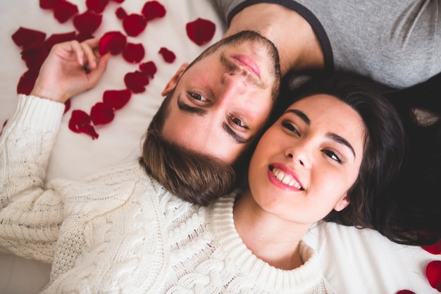 Couple smiling and lying on the bed head with head surrounded by rose petals