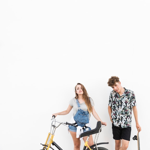 Free photo couple standing with bicycle and skateboard on white background