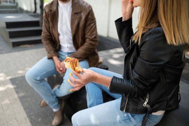 Free photo couple in synthetic leather jackets having a snack outdoors