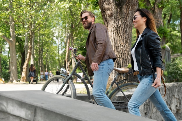 Free photo couple in synthetic leather jackets walking outdoors with bicycles