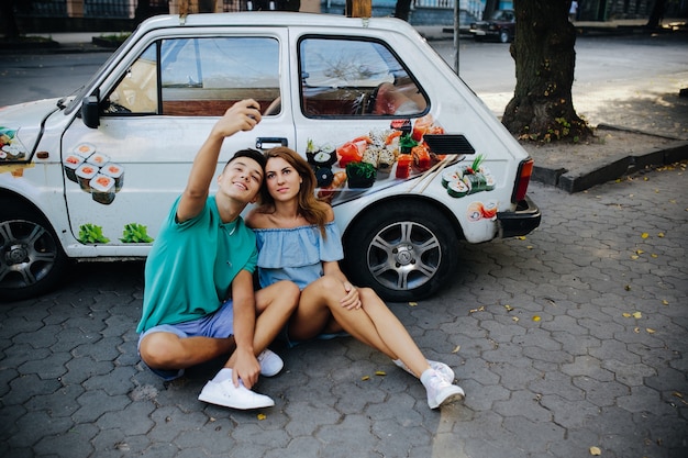 Couple taking selfie sitting against car