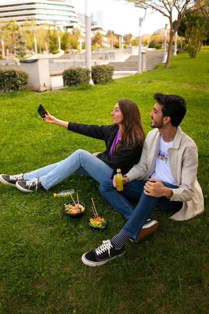 Couple taking selfie while eating bowl of salmon on the grass