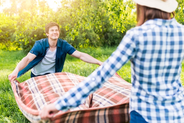 Free photo couple unfolding picnic blanket