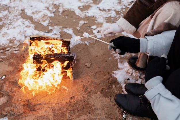 Couple up roasting marshmallows on the fire while on a winter road trip on the beach