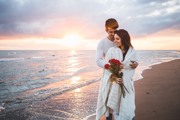 Couple walking on the beach with a bouquet of roses at sunset