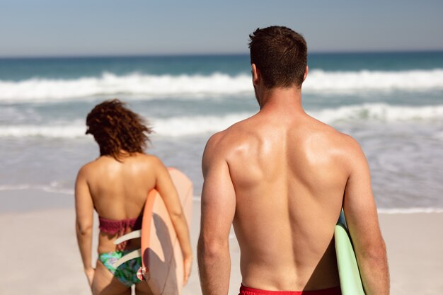 Couple walking with surfboard on beach in the sunshine