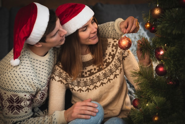 Free photo couple wearing santa hats decorating christmas tree