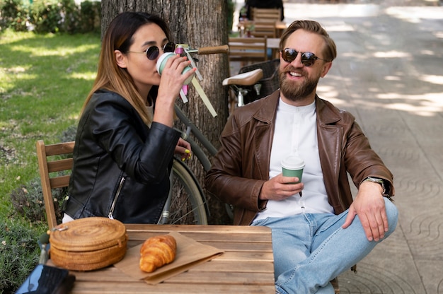 Free photo couple wearing synthetic leather jackets having coffee together outdoors