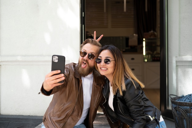 Free photo couple wearing synthetic leather jackets taking selfie together outdoors