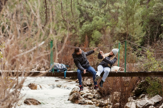 Free Photo couple with backpack sitting on bridge