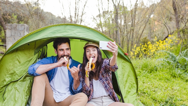 Couple with bananas taking selfie near tent