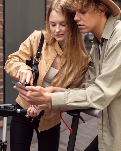 Free Photo couple with electric scooters  and smartphone outdoors