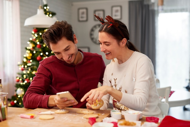 Couple with mobile phone decorating Christmas cookies