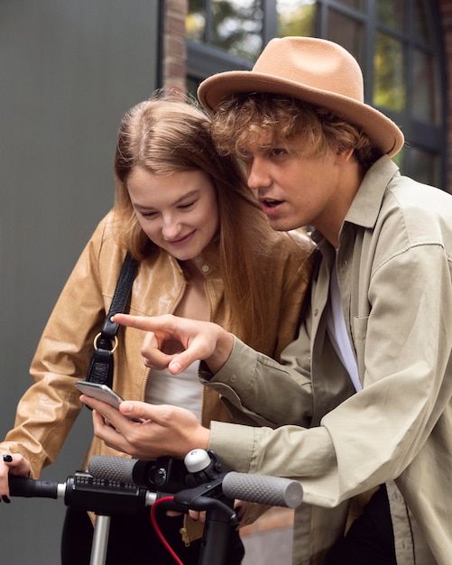 Free Photo couple with smartphone and electric scooters outdoors