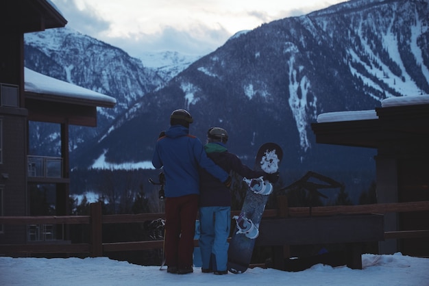 Free photo couple with snowboard standing on snow covered field