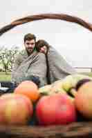 Free photo couple wrapped in one blanket sitting in front of fruits basket