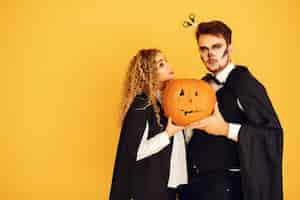 Free photo couple on a yellow background. woman wearing black costume. lady with halloween makeup.