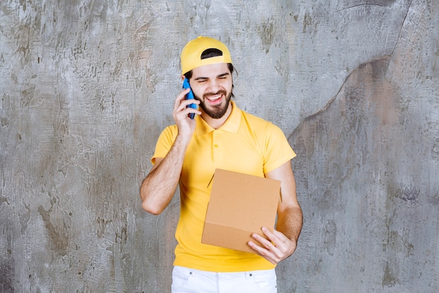 Free photo courier in yellow uniform holding an open cardboard box and taking orders via phone