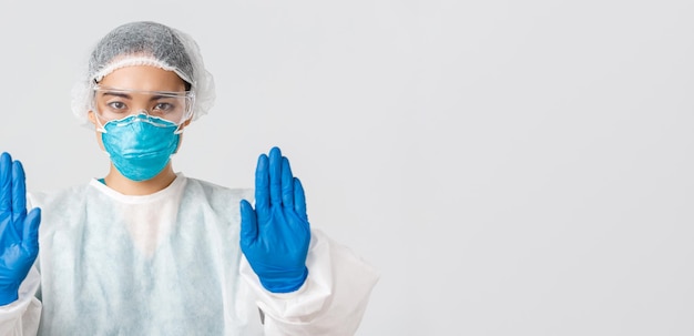 Covid-19, coronavirus disease, healthcare workers concept. Close-up of serious-looking concerned asian female doctor in personal protective equipment show stop gesture, prohibit enter dangerous zone