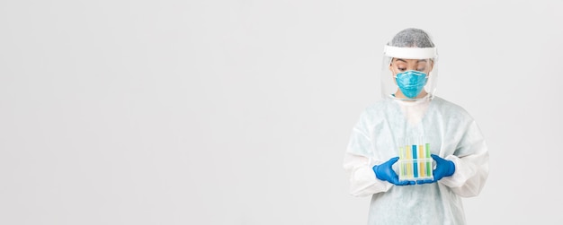 Free Photo covid-19, coronavirus disease, healthcare workers concept. excited asian female doctor, tech lab in personal protective equipment holding test-tubes with vaccine or analyses, white background.