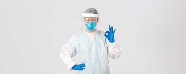 Free photo covid-19, coronavirus disease, healthcare workers concept. serious-looking professional female asian doctor in personal protective equipment, showing okay gesture, ensure safety of patient.