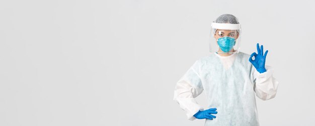 Free photo covid-19, coronavirus disease, healthcare workers concept. serious-looking professional female asian doctor in personal protective equipment, showing okay gesture, ensure safety of patient