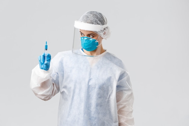 Covid-19, medical research, diagnosis, healthcare workers and quarantine concept. Professional doctor in personal protective equipment, PPE costume, holding syringe with coronavirus vaccine