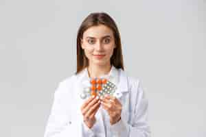 Free photo covid-19, preventing virus, health, healthcare workers and quarantine concept. physician in medical white scrubs, attractive female doctor showing medicine, different pills, smiling as recommend it