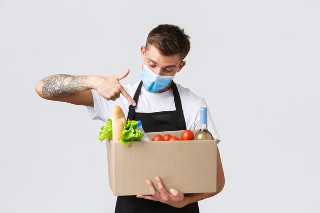 Covid contactless shopping and groceries delivery concept handsome salesman in medical mask pointing...